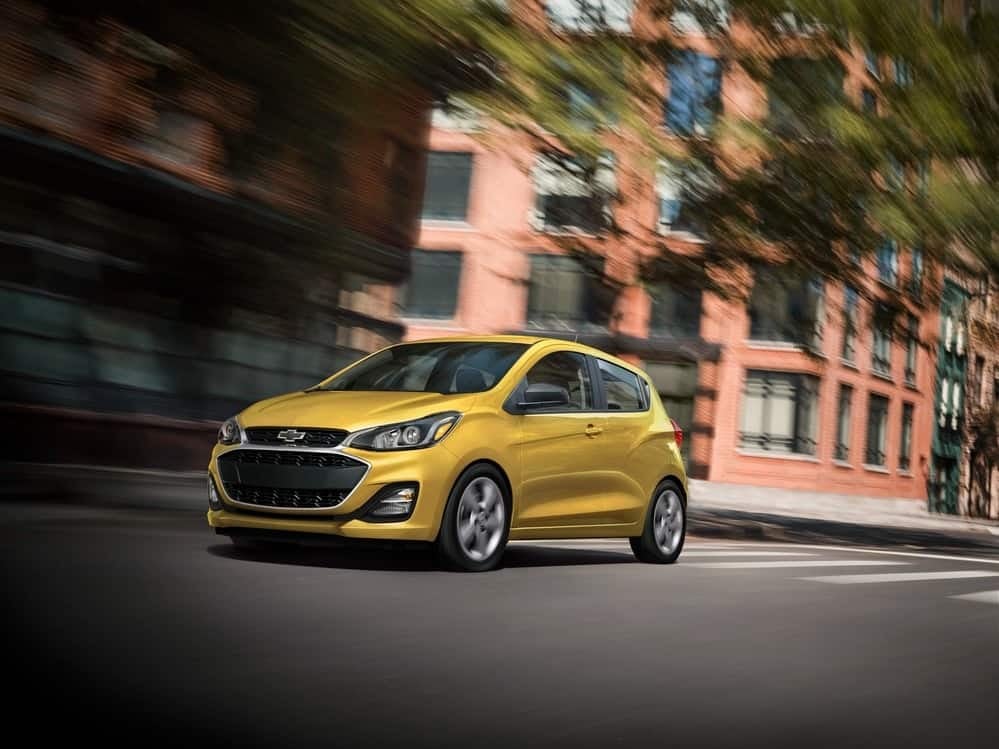 A yellow 2022 Chevy Spark drives through the city